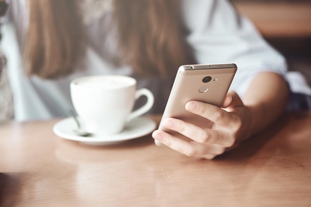 Mãos de mulher de negócios usando telefone inteligente e xícara de café