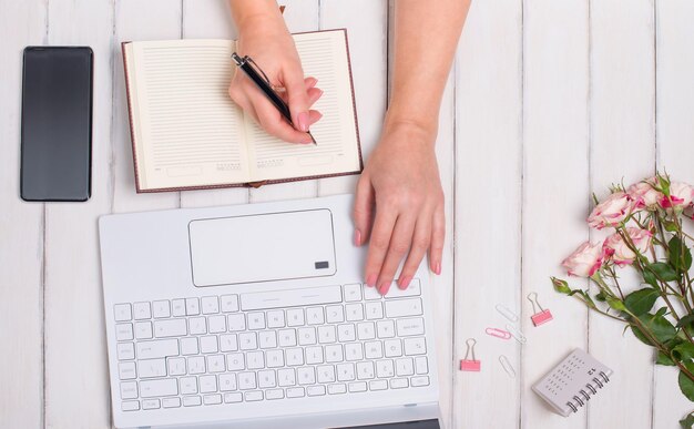 Mãos de mulher digitando laptop e escrevendo na agenda Conceito de espaço de trabalho feminino