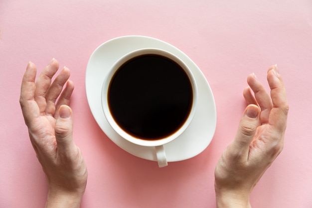 Mãos de mulher e uma xícara de café sobre fundo rosa, flat leigos