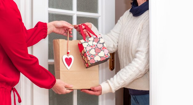 Mãos de mulher entregando sacola de compras com corações vermelhos do dia dos namorados e caixas de presentes do trabalhador do serviço de entrega.