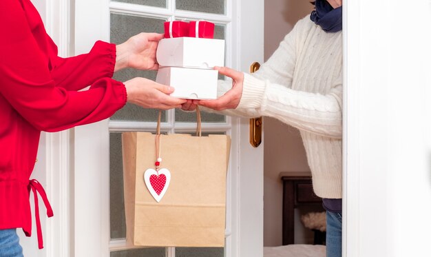 Mãos de mulher entregando sacola de compras com corações vermelhos do dia dos namorados e caixas de presentes do trabalhador do serviço de entrega.