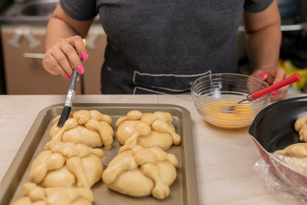 Mãos de mulher envernizando o pão dos mortos que ela está preparando para assar