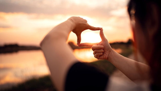 Mãos de mulher fazendo gesto de quadro com pôr do sol