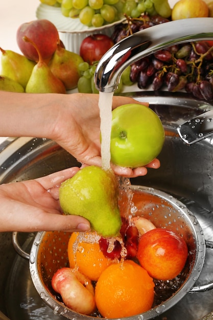 Mãos de mulher lavando maçã e outras frutas em peneira na pia