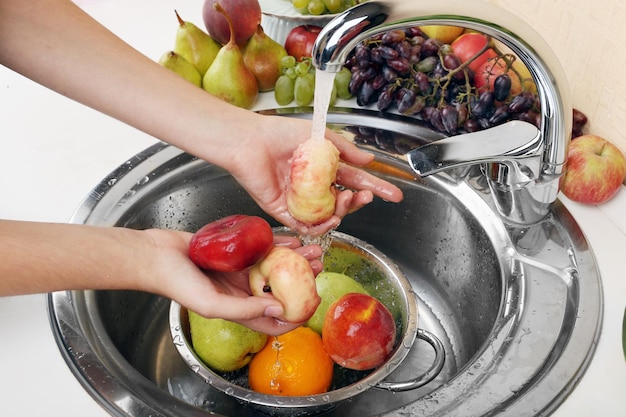 Foto mãos de mulher lavando pêssegos e outras frutas em peneira na pia