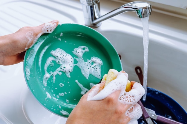 Mãos de mulher lavando prato na pia da cozinha