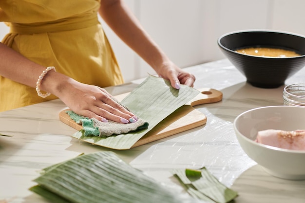 Mãos de mulher limpando folhas de bananeira ao cozinhar bolo de arroz em casa