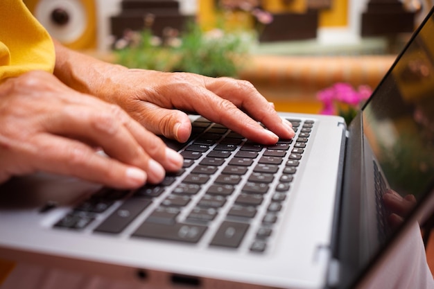 Mãos de mulher madura digitando no teclado do laptop navegando na net