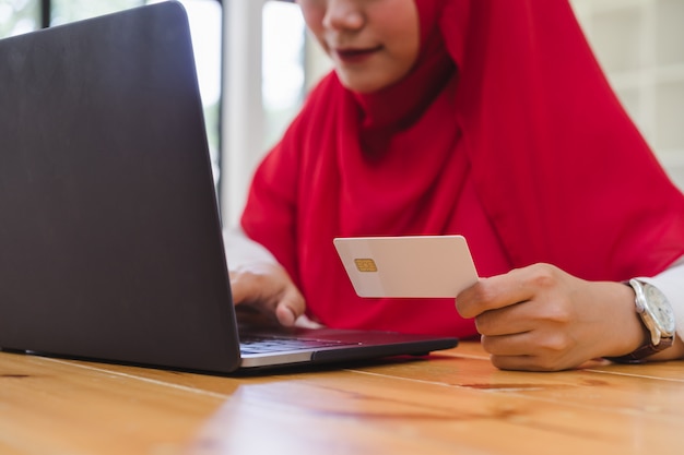 Mãos de mulher muçulmana segurando o cartão de crédito e usando o laptop para compras on-line. sexta-feira negra e cyber segunda-feira compras online conceito