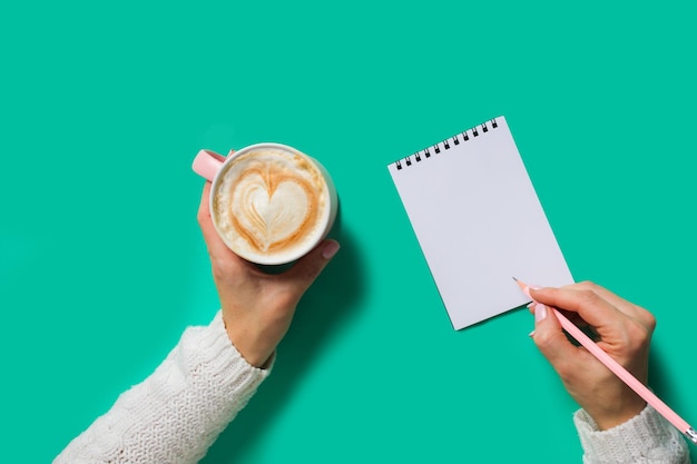 Mãos de mulher no suéter branco fazendo planos Vista superior xícara de cappuccino na mão Copiar espaço