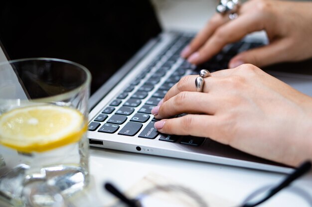 Mãos de mulher no teclado do laptop, local de trabalho aconchegante