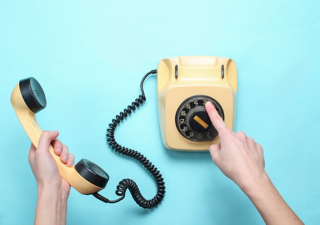 Mãos de mulher pega o número do telefone rotativo e mantém o aparelho no fundo azul pastel. vista superior, minimalismo