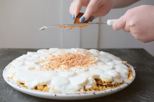 mãos de mulher ralando chocolate na torta de Banoffee com bananas chantilly chocolate e caramelo torta de banoffee caseira