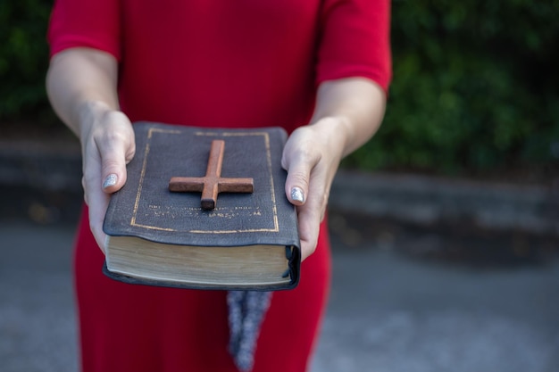 Mãos de mulher rezando a Deus com cruz de madeira