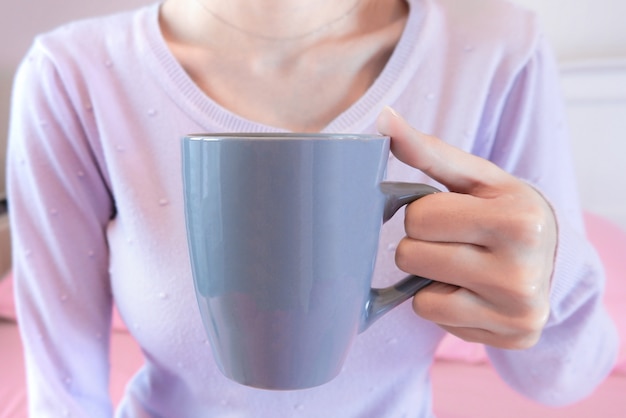 Mãos de mulher segurando a xícara de café. Menina na camisola segurando caneca.