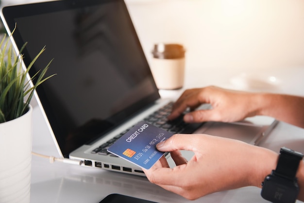 Mãos de mulher segurando cartão de crédito e usando laptop com compra de produtos em casa