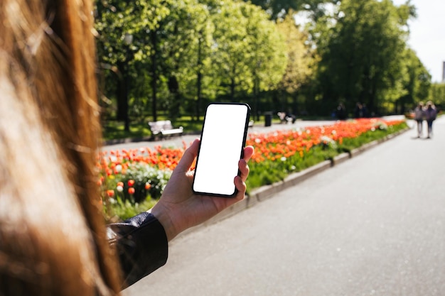 Mãos de mulher segurando e usando telefone inteligente com fundo de jardim de flores coloridas turva