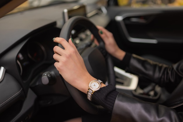 Mãos de mulher segurando o volante de um carro novo no showroom.