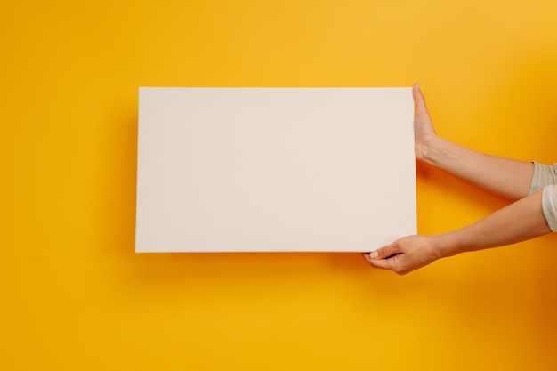 Mãos de mulher segurando papel de tela branca em branco com copyspace no banner de folha vazia de fundo amarelo