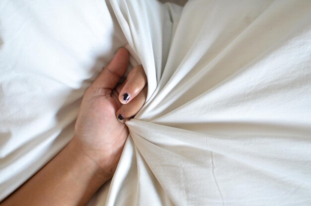 Mãos de mulher segurando preservativo e dinheiro em rupia indonésia em uma cama debaixo do cobertor foto