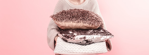 Mãos de mulher segurando três travesseiros modernos para parede de parede sofá-de-rosa na tendência, minimalismo conceito casa aconchegante limpo