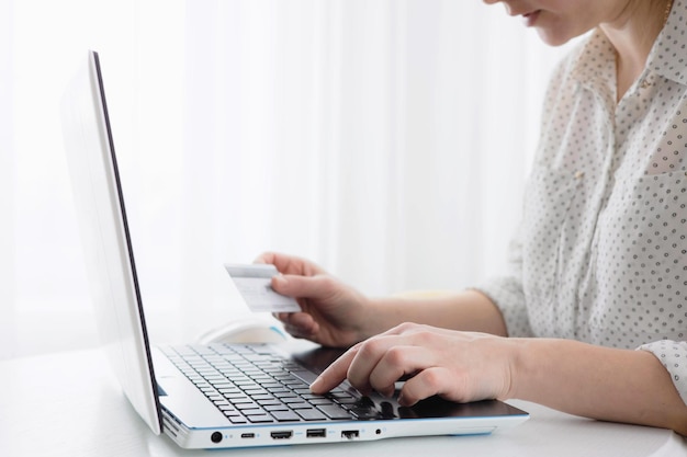 Mãos de mulher segurando um cartão de crédito e usando o computador portátil em casa Conceito de compra online. Foco seletivo.