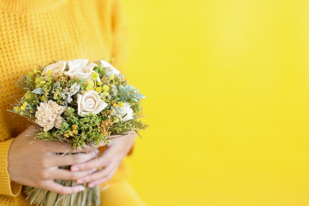 Mãos de mulher segurando um lindo buquê com flores frescas em fundo amarelo com espaço de cópia