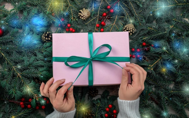 Mãos de mulher segurando um presente de natal ou caixa de presente decorada árvore de abeto e luzes de natal Preparando-se para feriados e celebração Mãos femininas segurando presente ou caixa de presente