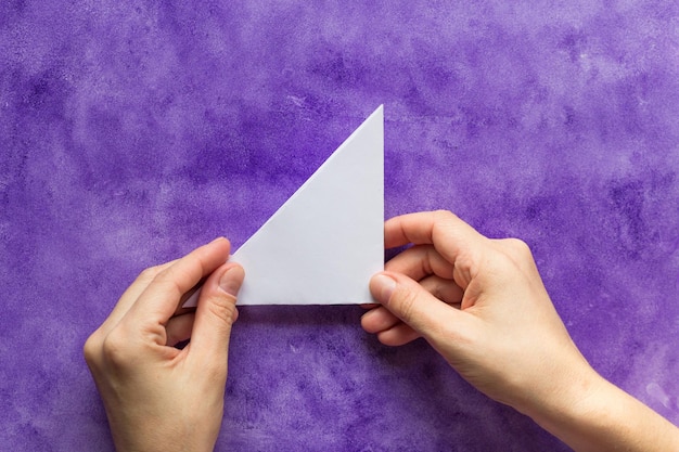 Mãos de mulher segurando um triângulo de papel dobrado na superfície violeta
