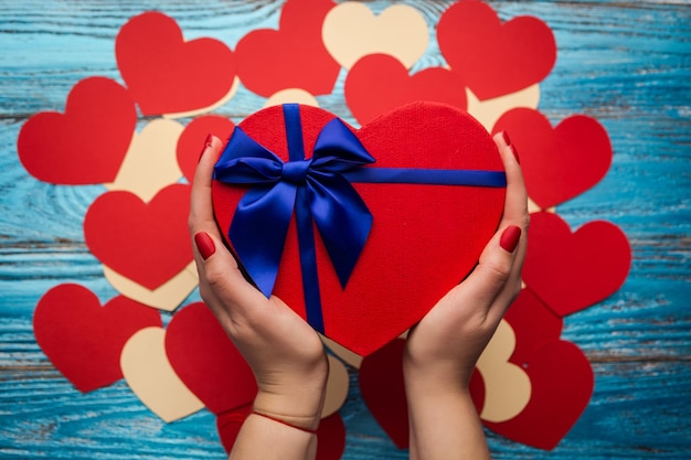 Mãos de mulher segurando uma caixa de presente na forma de um coração de fundo de dia dos namorados