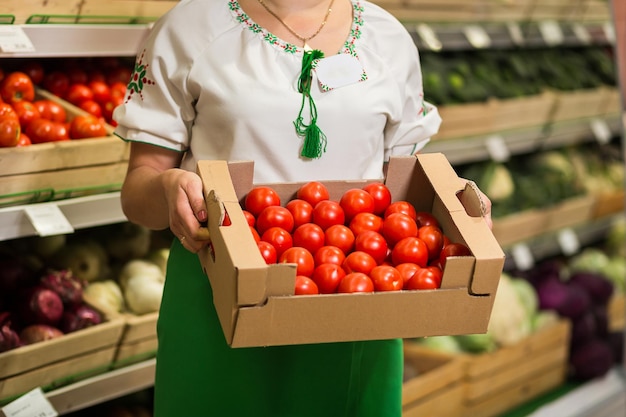 Mãos de mulher segurando uma grande caixa de colheita de tomate no mercado