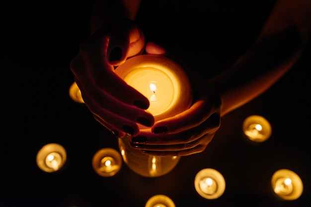 Mãos de mulher segurando uma vela acesa. Muitas chamas de velas brilhando. Fechar-se.