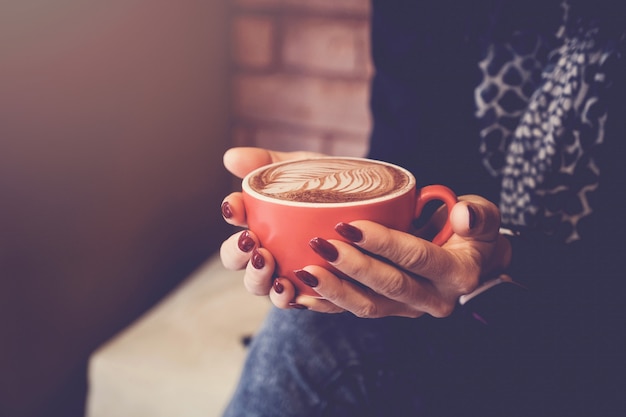 Mãos de mulher segurando uma xícara de café com leite vermelho, relaxante, pensando, conceito de reunião de negócios