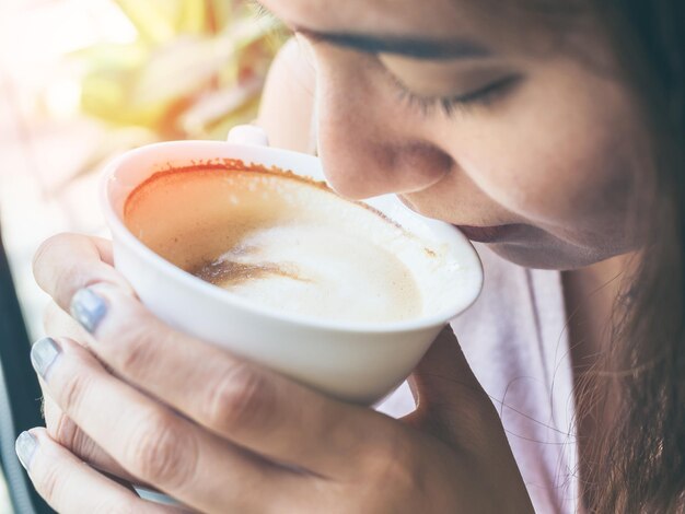 Mãos de mulher segurando uma xícara de café quente branco