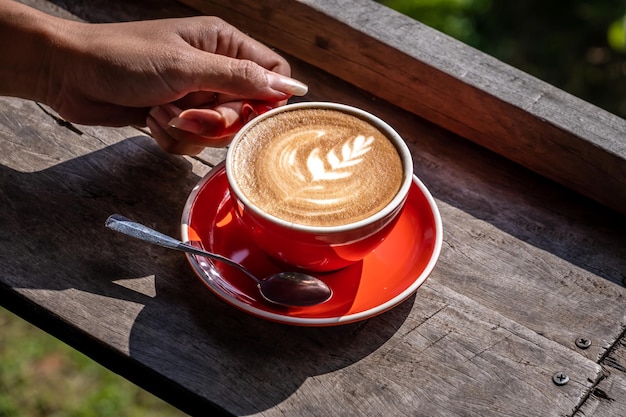 Mãos de mulher segurando uma xícara laranja de arte de café