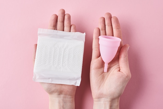 Mãos de mulher segurar absorvente e copo menstrual em rosa