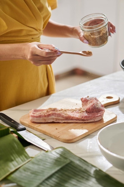 Mãos de mulher temperando carne de porco ao fazer bolo quadrado