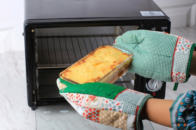 Mãos de mulher tomando assadeira clara com espaguete brulee (espaguete assado) fora do forno. Foco Selecionado