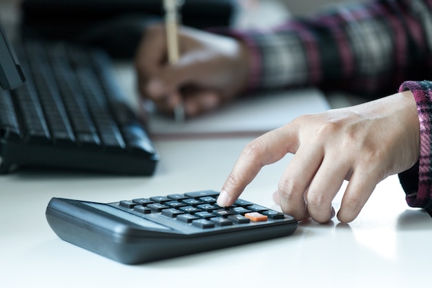 Mãos de mulher usando calculadora na mesa