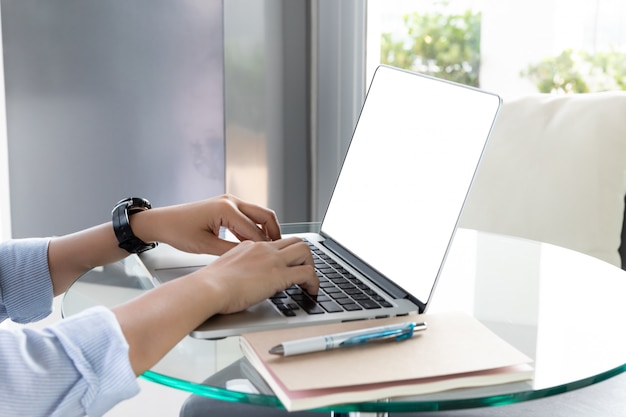 Mãos de mulher usando laptop com tela em branco na mesa de vidro no escritório em casa