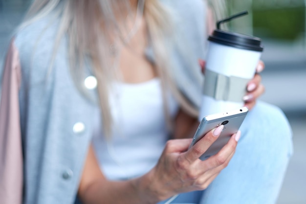 Mãos de mulher usando telefone e segurando um copo de papel com café teen hipster online conceito de internet