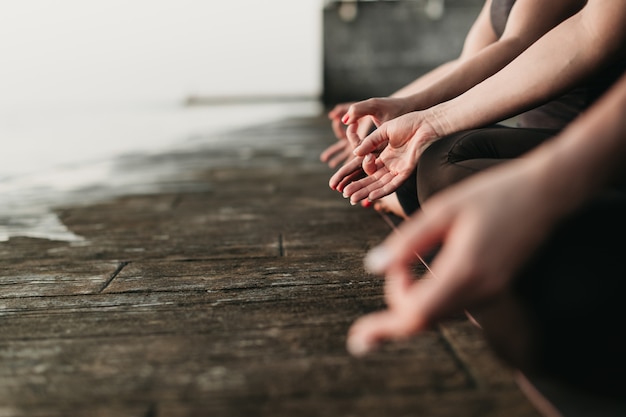 Mãos de mulheres meditando ao ar livre perto do mar, sentado no tapete de ioga