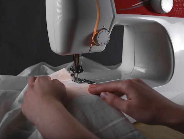 Mãos de mulheres na máquina de costura durante o processo de trabalho com o pano.