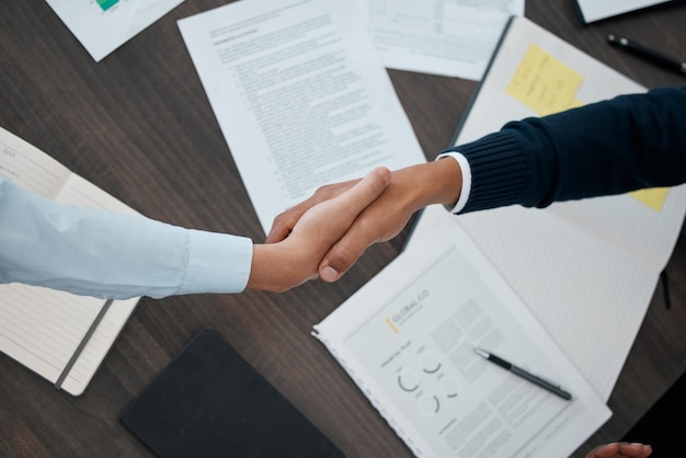 Foto mãos de negócios e aperto de mão com documentos acima da papelada para contrato de trabalho ou análise no escritório mão de pessoas em parceria tremendo para boas-vindas do contrato corporativo ou reunião b2b