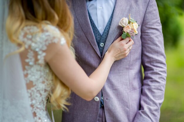 Mãos de noivas prendendo uma pequena flor na lapela para o noivo Decoração tradicional floral para o noivo um acessório no terno de casamento festivo Closeup