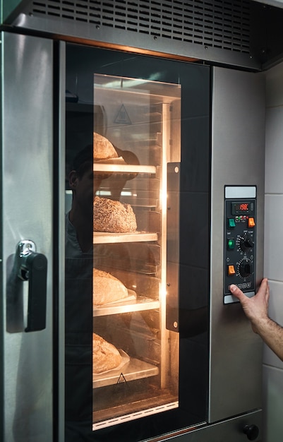 mãos de padeiro tocando um botão no forno com muito pão fresco dentro.