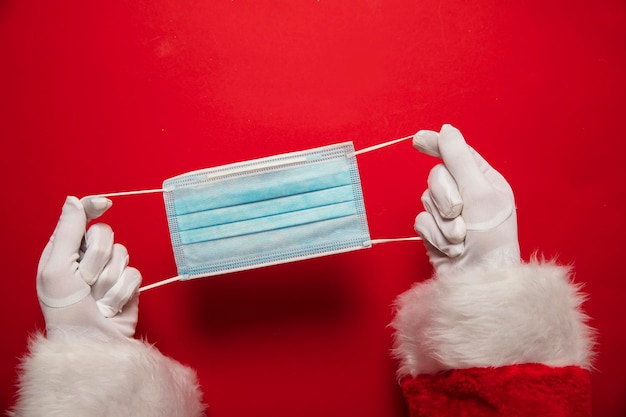 Mãos de papai noel segurando uma máscara facial cirúrgica de coronavírus natal covid