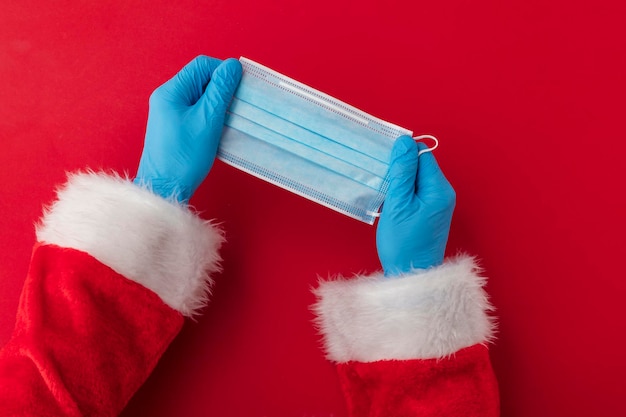 Mãos de papai noel segurando uma máscara facial cirúrgica de coronavírus natal covid