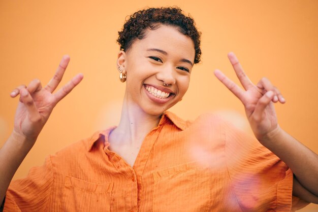 Foto mãos de paz e mulher feliz no estúdio com gesto de agradecimento e amor próprio contra o rosto de liberdade de espaço de fundo laranja e modelo feminino com sinal v emoji para confiança de bom humor ou positividade