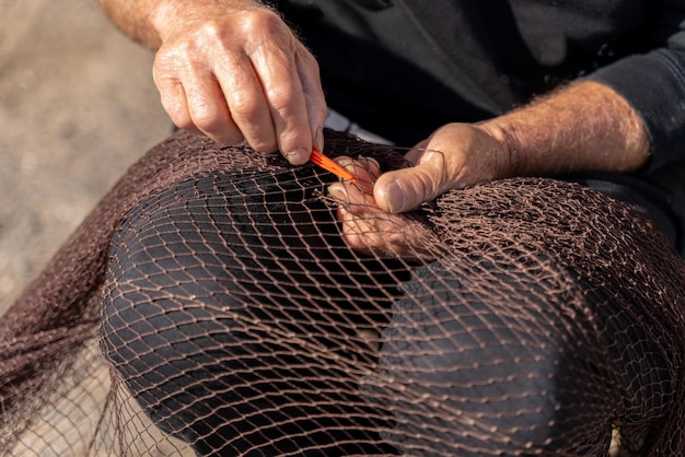 Mãos de pescador costurando uma rede de pesca